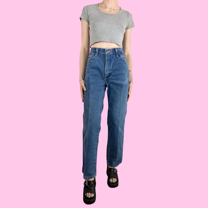 May include: A person wearing a gray crop top and blue denim jeans. The jeans have a high waist and a straight leg fit. The person is also wearing black platform sandals.