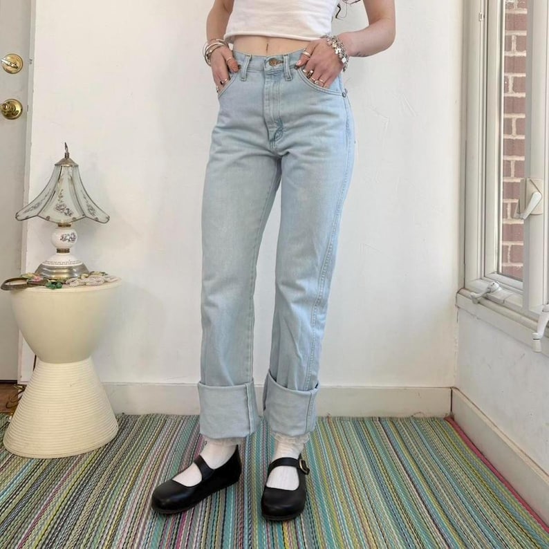 Op de afbeelding: Lichtblauwe denim jeans met omgeslagen zomen. De jeans worden gecombineerd met zwarte Mary Jane schoenen en witte sokken. Een casual outfit, geschikt voor dagelijks gebruik.
