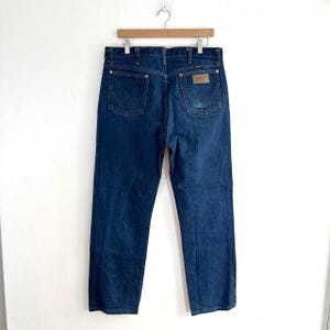 May include: A pair of dark blue denim jeans with a brown leather patch on the back pocket that says "Wrangler".