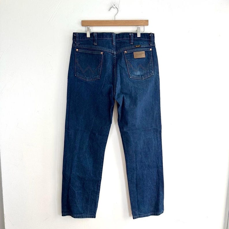 May include: A pair of dark blue denim jeans with a brown leather patch on the back pocket that says "Wrangler".