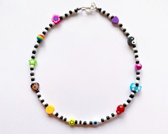 May include: A black and white beaded necklace with colourful charms, including a rainbow, a flower, a star, a heart, a yin yang symbol, a smiley face, an evil eye, a bow, a strawberry, and an orange slice.