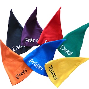 Könnte beinhalten: Eine Sammlung von sieben bunten, spitz zulaufenden Hüten, jeweils in einer anderen Farbe: Schwarz, Lila, Rot, Grün, Blau, Orange und Gelb. Jeder Hut hat einen Namen in Weiß gestickt. Die Hüte sind kreisförmig angeordnet.