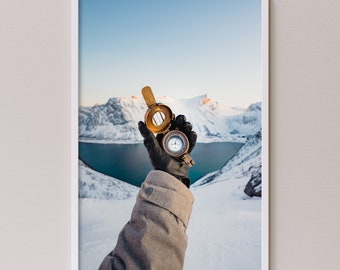 Winter in the mountains of Senja, Norway print. Person holding a compass between the famous snow covered peaks. Photography by Simon Migaj