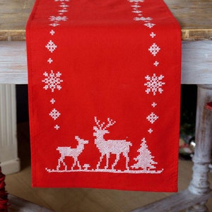 May include: Red table runner with white embroidered snowflakes and a reindeer family design. The runner is perfect for a Christmas table setting.
