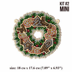 May include: A wooden Christmas wreath with a green and white design, featuring a red berry and a brown bird. The wreath is 7.09 inches by 6.93 inches and is labeled "KIT #2 MINI".