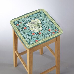 May include: A wooden bar stool with a green and white floral patterned cushion. The cushion has a green border with a light green and orange trim.