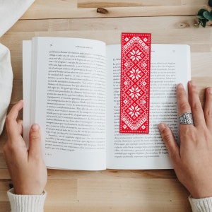May include: A red and white bookmark with a geometric pattern. The bookmark is made of fabric and has a fringed edge.