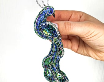 Puede incluir: Un broche de pavo real azul y verde con pedrería iridiscente y un diseño de alambre plateado.