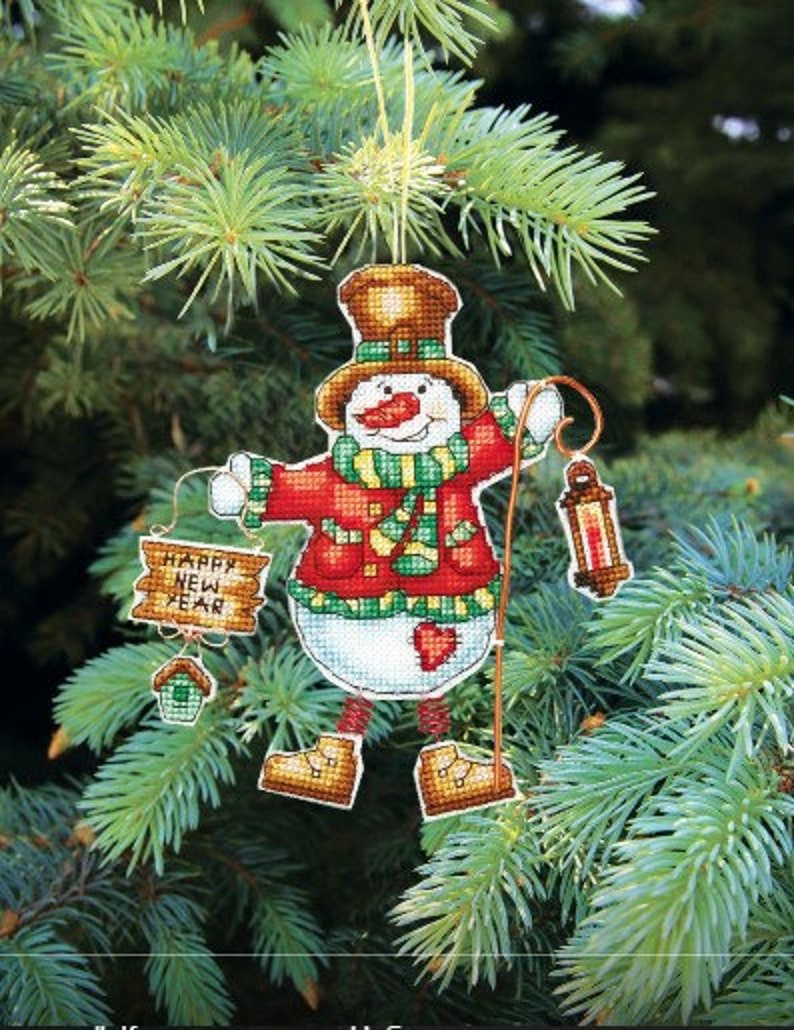 May include: A snowman Christmas ornament with a red and green scarf, a red hat, and a sign that says "Happy New Year".