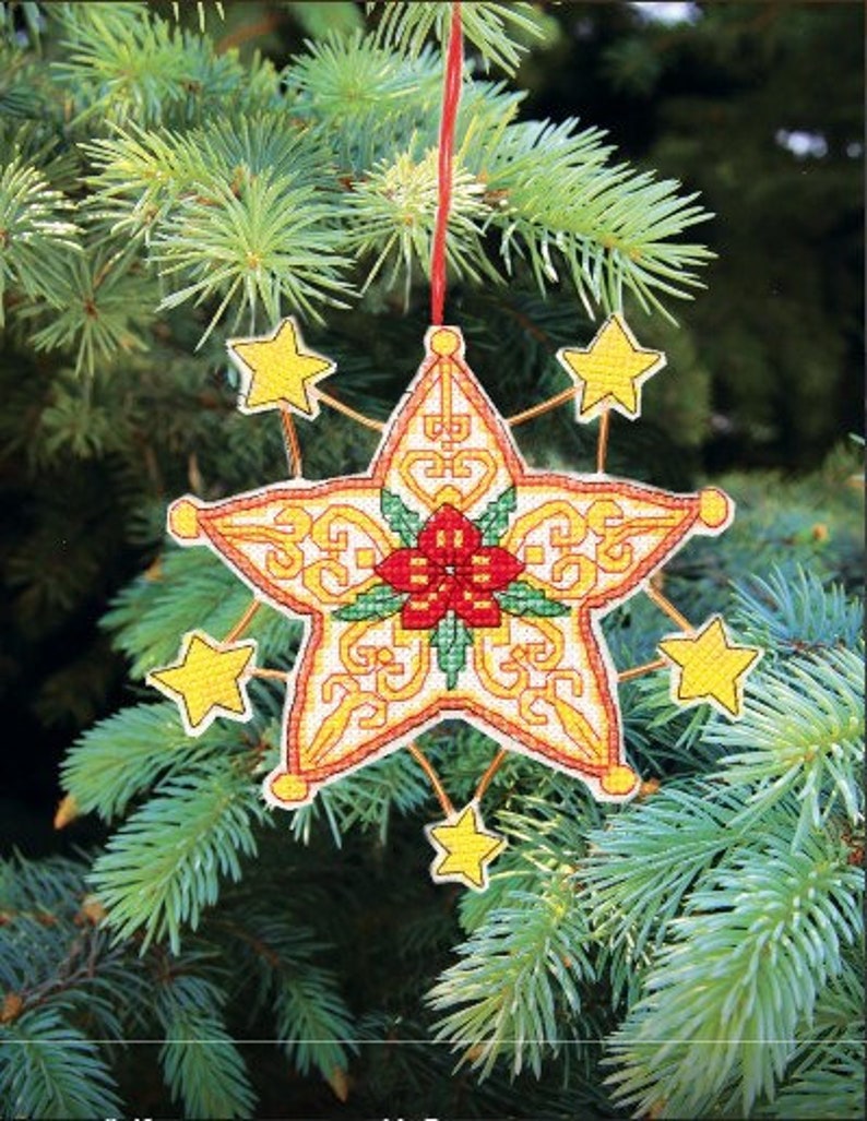 May include: A yellow star-shaped Christmas ornament with a red poinsettia in the center. The ornament has a gold and white pattern and is hanging from a red string.