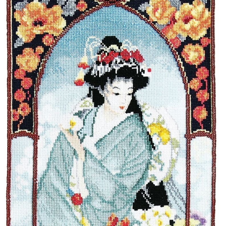 Op de afbeelding: Een borduurwerk met kruissteek van een vrouw in een blauwe kimono met een bloemenpatroon. Ze draagt ​​een rood-witte hoofdband en heeft zwart haar. De achtergrond is lichtblauw met een bloemige rand.