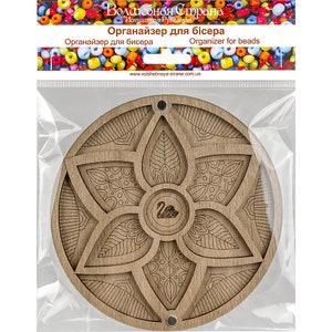 May include: A wooden bead organizer with a floral design. The organizer has six compartments and a swan logo in the center. The text "Organizer for beads" is printed on the packaging.