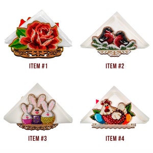 May include: Four wooden napkin holders with different embroidered designs. The first holder features a red rose, the second has two red birds, the third has two bunnies, and the fourth has a chicken with eggs.