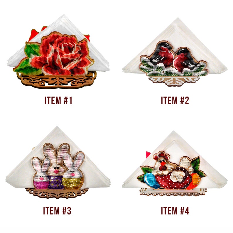 May include: Four wooden napkin holders with different embroidered designs. The first holder features a red rose, the second has two red birds, the third has two bunnies, and the fourth has a chicken with eggs.