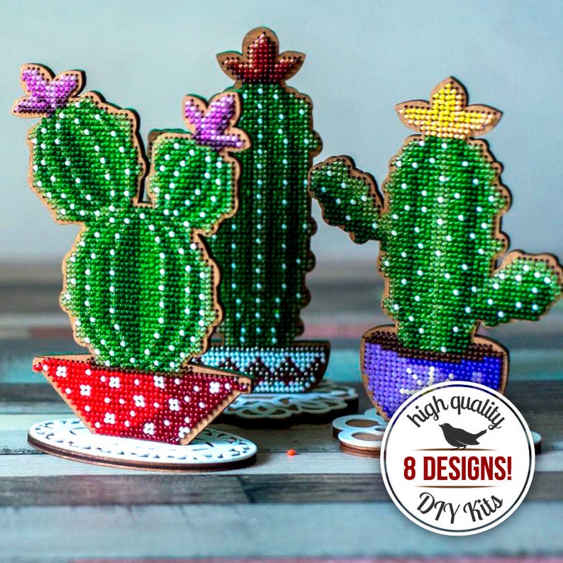May include: Three decorative cactus figures with green cross-stitch detailing and white polka dots. Each cactus is in a colorful pot, with a wooden base. The image includes a circular logo with the text "high quality 8 DESIGNS! DIY Kits".