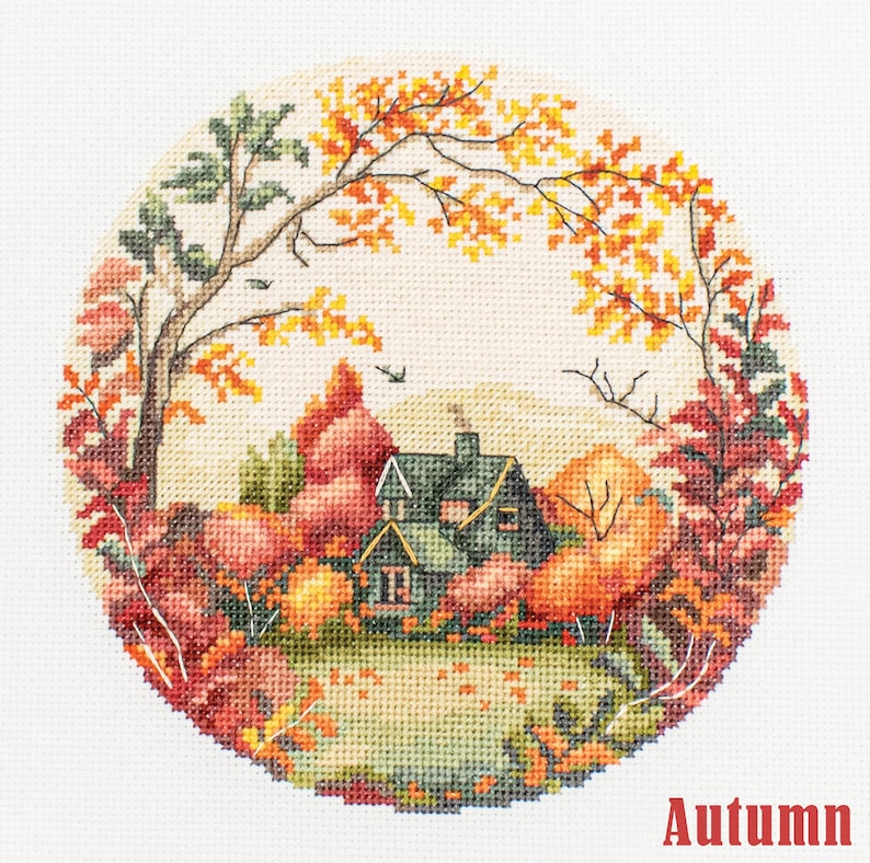 May include: A cross-stitch pattern featuring a cozy cottage nestled in a colorful autumn forest. The scene is surrounded by a circle of vibrant red, orange, and yellow leaves. The text "Autumn" is printed below the image.