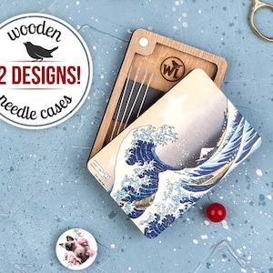 May include: A wooden needle case with a design of The Great Wave off Kanagawa by Hokusai. The case is open and shows a set of needles inside. The case is made of wood and has a natural finish. The design is printed on the front of the case. The case is closed with a magnetic clasp. The case is part of a set of 12 different designs.