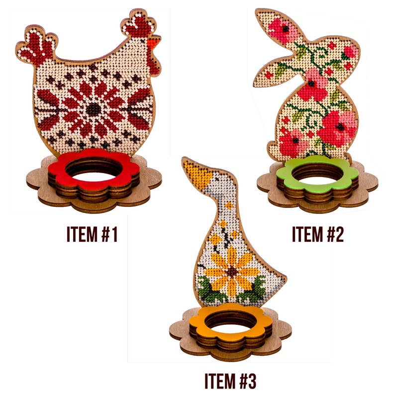 Pu&ograve; includere: Tre porta uova di Pasqua in legno, ognuno con un diverso design ricamato: un pollo rosso e bianco, un coniglietto rosa e verde e un'oca gialla e verde. Ogni porta uova ha un'apertura circolare per un uovo e una base a forma di fiore.