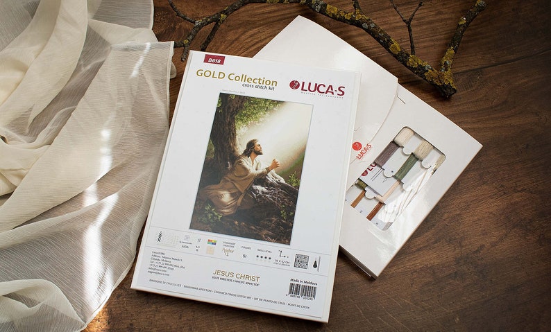 May include: A cross-stitch kit featuring a painting of Jesus Christ praying in a woodland setting. The kit includes white fabric, floss, and instructions. The kit is labelled "GOLD Collection" and "JESUS CHRIST".