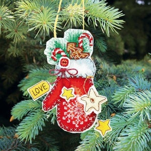 May include: A red felt Christmas ornament shaped like a mitten with white snowflakes and a white star. The mitten has a white cuff with a green and white candy cane and a white bow. The ornament has a yellow tag that says "LOVE" and a yellow string for hanging.