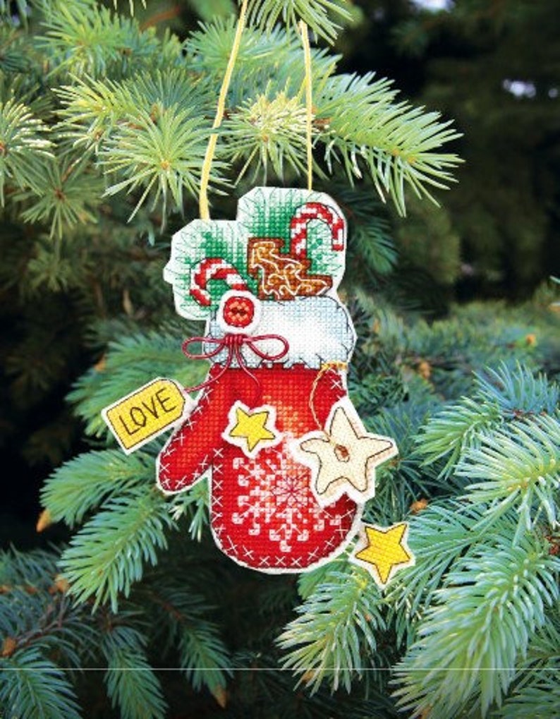 May include: A red felt Christmas ornament shaped like a mitten with white snowflakes and a white star. The mitten has a white cuff with a green and white candy cane and a white bow. The ornament has a yellow tag that says "LOVE" and a yellow string for hanging.