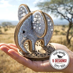 Op de afbeelding: Houten olifantenbeeldje met parel- en strassversieringen. De olifant staat op een decoratieve houten basis. Een cirkelvormige afbeelding toont "hoge kwaliteit" en "5 DESIGNS! DIY Kits".