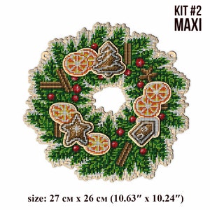May include: A Christmas wreath with a wooden base, decorated with green pine branches, red berries, cinnamon sticks, and orange slices. The wreath also features gingerbread cookies and a small wooden house. The wreath is 10.63 inches by 10.24 inches.