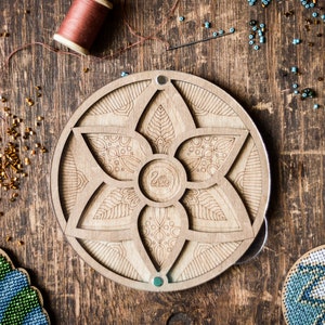 May include: A wooden bead organizer with a circular design featuring a flower with six petals. The organizer has a small compartment in the center and five larger compartments around the edge. The organizer is made of light brown wood and has a natural finish.