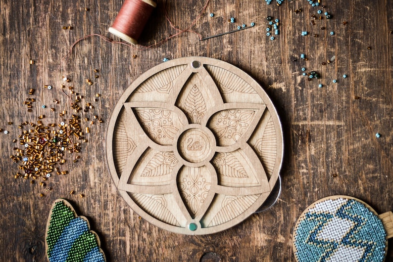 May include: A wooden bead organizer with a circular design featuring a flower with six petals. The organizer has a small compartment in the center and five larger compartments around the edge. The organizer is made of light brown wood and has a natural finish.
