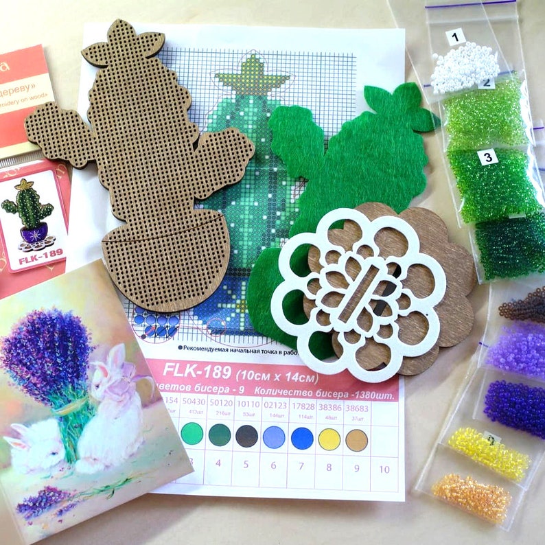 May include: Crafting kit with wooden cactus and flower shapes, green felt cutouts, and a cross-stitch pattern. Includes small bags of beads in various colors, a card with lavender and rabbits, and a card with a cactus.