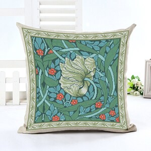 May include: A decorative pillow with a floral design featuring a large white flower with green leaves and orange flowers on a teal background. The pillow has a beige border with a green and white pattern.
