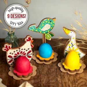 Può includere: Tre porta uova di Pasqua in legno, ognuno con un design diverso: una gallina, un uccello e un'anatra. I porta uova sono decorati con perline colorate e hanno uno spazio per posizionare un uovo al centro. Il testo "high quality 9 DESIGNS! DIY kits" è visibile nell'immagine.