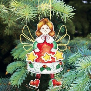 May include: A cross-stitch ornament featuring a red-dressed angel with gold wings and a holly wreath. The angel is holding a star in each hand and is wearing ice skates.