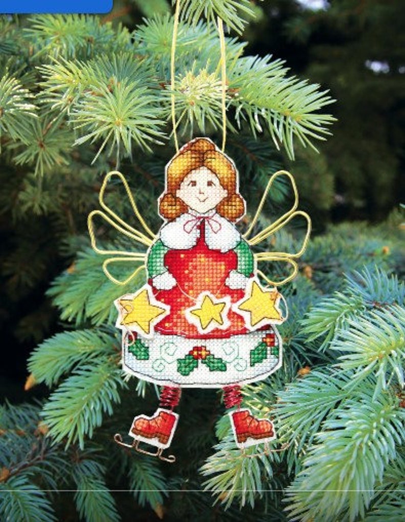 May include: A cross-stitch ornament featuring a red-dressed angel with gold wings and a holly wreath. The angel is holding a star in each hand and is wearing ice skates.