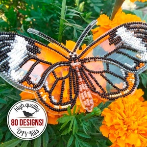 May include: A beaded butterfly with black, white, orange, and brown beads on a clear plastic background. The butterfly is sitting on top of orange marigold flowers. The image also includes a circular sticker with the text "high quality 80 DESIGNS! DIY Kits".