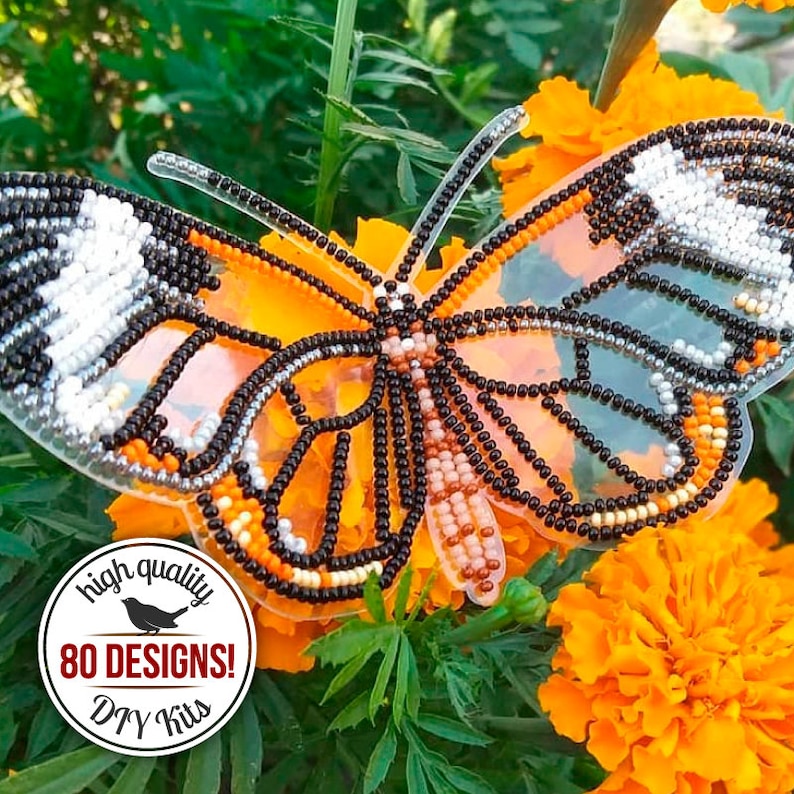 May include: A beaded butterfly with black, white, orange, and brown beads on a clear plastic background. The butterfly is sitting on top of orange marigold flowers. The image also includes a circular sticker with the text "high quality 80 DESIGNS! DIY Kits".