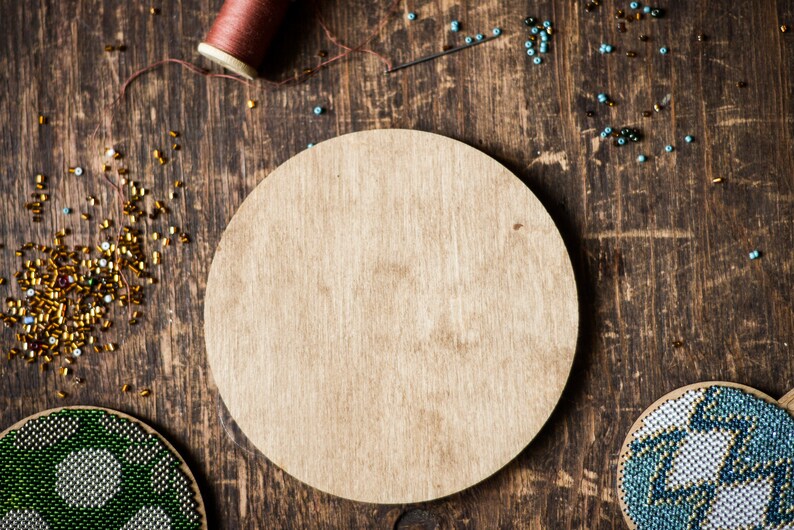 May include: A wooden round craft base with a natural wood finish. The base is surrounded by colorful beads and a spool of thread.