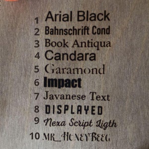 May include: A close-up of a wooden board with a list of 10 different fonts, numbered 1 through 10. The fonts are: Arial Black, Bahnschrift Cond, Book Antiqua, Candara, Garamond, Impact, Javanese Text, DISPLAYED, Nexa Script Ligth, and MR HONEY BEEG.