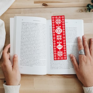 May include: Red and white Christmas-themed bookmark with a snowflake pattern and ornaments. The bookmark is made of fabric and has a fringed edge.