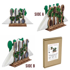 May include: A wooden napkin holder with a green and brown design featuring a variety of kitchen utensils. The holder is decorated with beads and has a cutout design around the edges. The holder is shown with a white napkin inside.