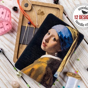 May include: A wooden needle case with a magnetic closure, featuring a reproduction of the famous "Girl with a Pearl Earring" painting. The case is made of wood and has a black background with a colorful image of the painting. The case is closed and has a small metal tag with the word "Veo" on it. The case is surrounded by beads and a pink measuring tape.