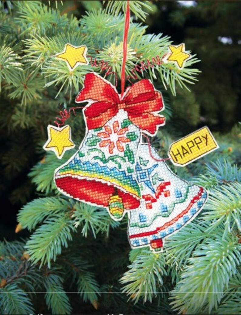 May include: Two red and white bells with a red bow and a yellow tag that says "HAPPY" hanging on a green Christmas tree.