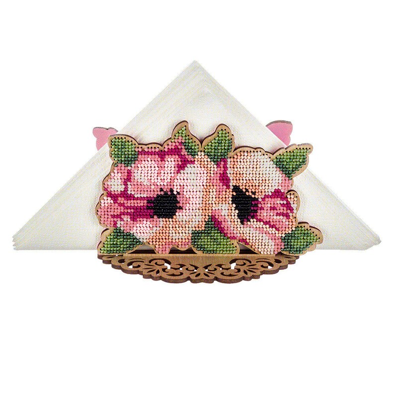 May include: A wooden napkin holder with a floral design. The design features two pink flowers with black centers and green leaves. The holder is made of wood and has a decorative edge.