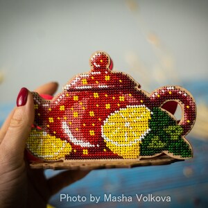 May include: A red and white beaded teapot with yellow lemons and green leaves. The teapot is a decorative tea bag holder.