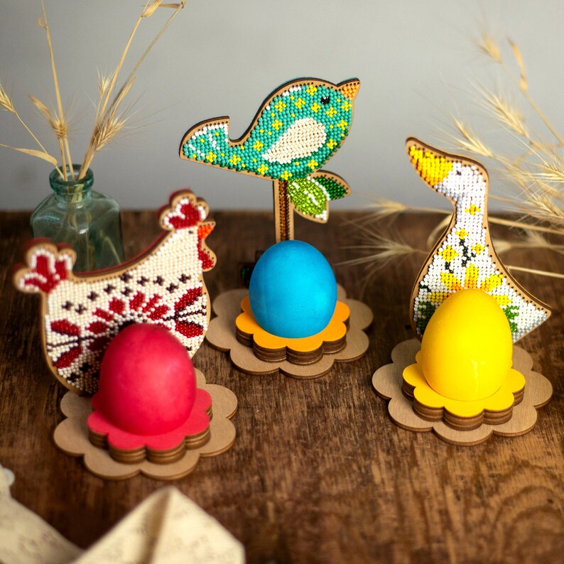 Pu&ograve; includere: Tre porta uova di Pasqua in legno, ognuno con un diverso design di animali perlati: un uccello blu, una gallina rosso e bianca e un'anatra gialla. Ogni porta uova contiene un piccolo uovo colorato.