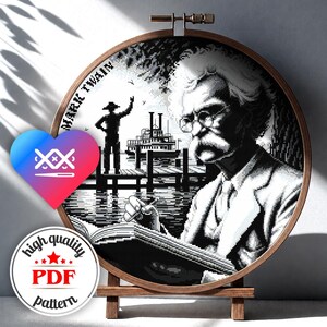 May include: A circular wooden embroidery hoop containing a black and white cross-stitch pattern of Mark Twain writing in a book, with a steamboat and a figure on a dock in the background. The text MARK TWAIN is visible on the left side of the design.