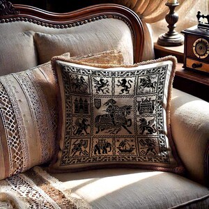 May include: Square cushion with a black and beige medieval design. The cushion features a repeating pattern of heraldic figures, castles, and a knight on horseback. It has a beige fringe trim and is on a cream-coloured armchair.