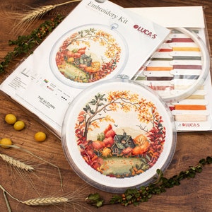 May include: Embroidery kit with a circular design of a house in a forest with autumn leaves. The kit includes a hoop, floss, and instructions. The kit is titled "The Autumn" and is by Lucas-S.