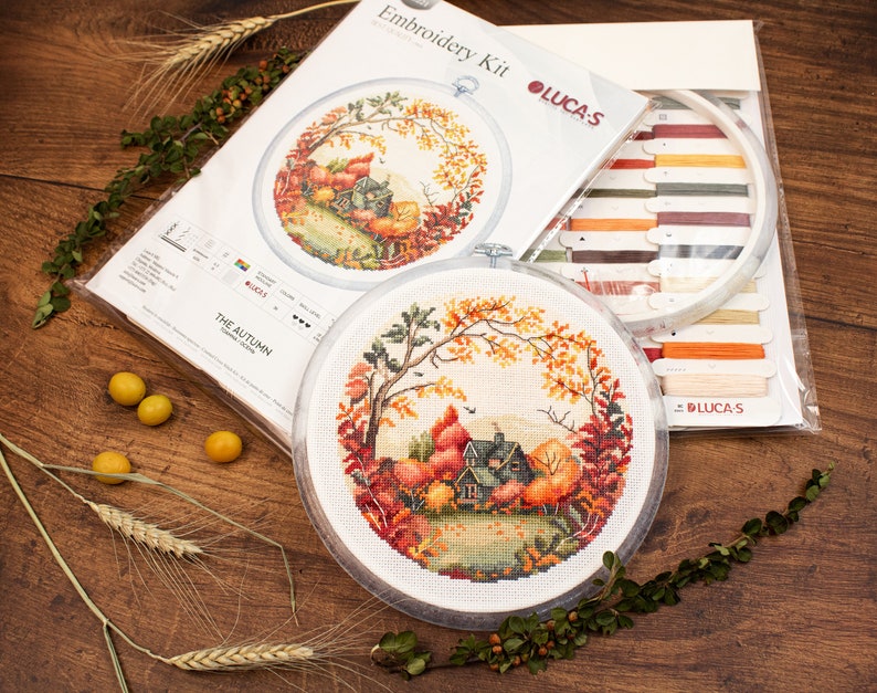 May include: Embroidery kit with a circular design of a house in a forest with autumn leaves. The kit includes a hoop, floss, and instructions. The kit is titled "The Autumn" and is by Lucas-S.