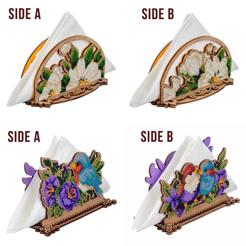 May include: Two wooden napkin holders with different designs. The first holder features a white floral design with green leaves. The second holder features two blue birds with purple flowers. Both holders have a white napkin inside.